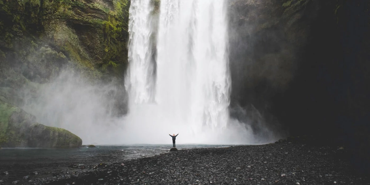 A huge waterfall in the background and a small figure standing at the bottom, raising their arms.