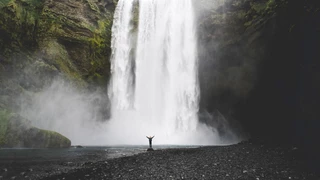 A huge waterfall in the background and a small figure standing at the bottom, raising their arms.