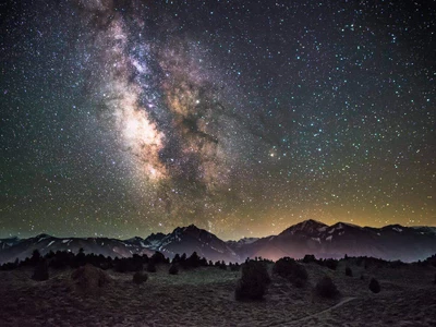 The milky way above a foggy landscape with mountains in the background and a forest in the foreground.